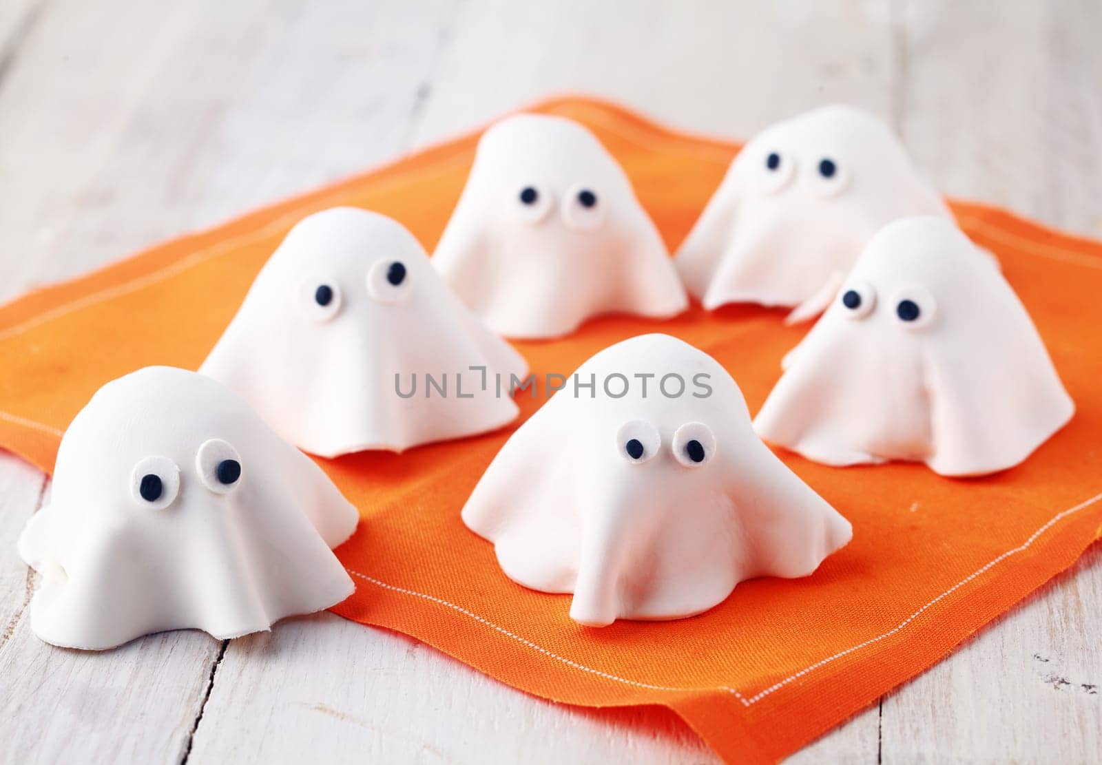 Scary white edible Halloween ghost appetizers for party snacks or treats for young children trick-or-treating on Allhallows Eve standing ready on a colorful orange napkin
