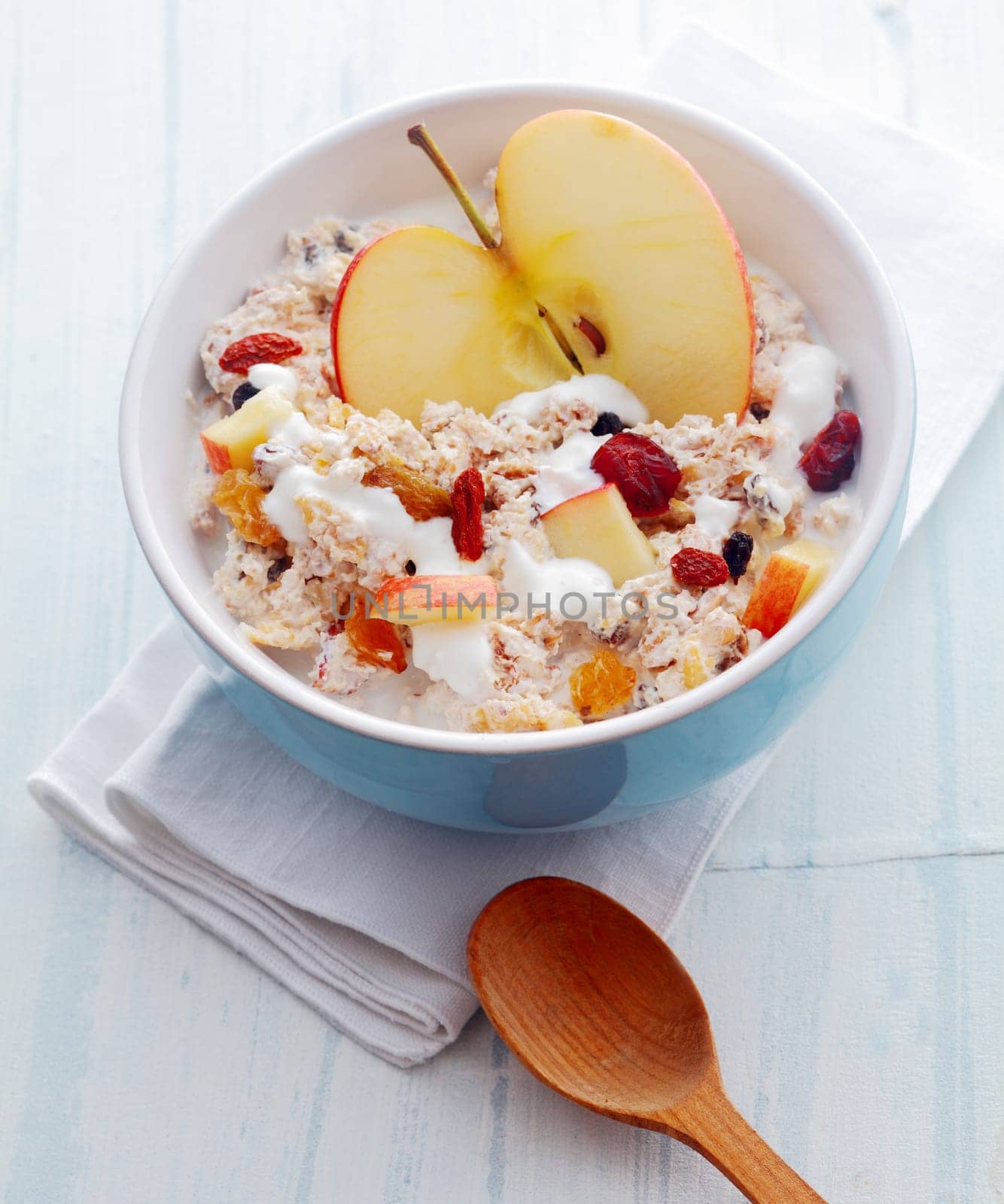 Delicious homemade muesli with fruit including fresh halved and diced apple and dried apricots and raisins and nuts served in a bowl on a white wooden rustic table