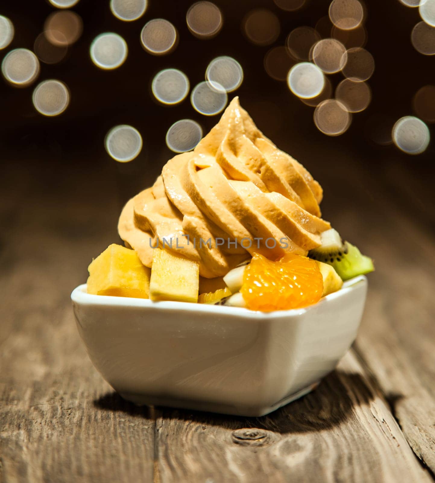 Macro Mouth Watering Yellow Frozen Yogurt on Assorted Fruit Slices on White Bowl Placed on Wooden Table.