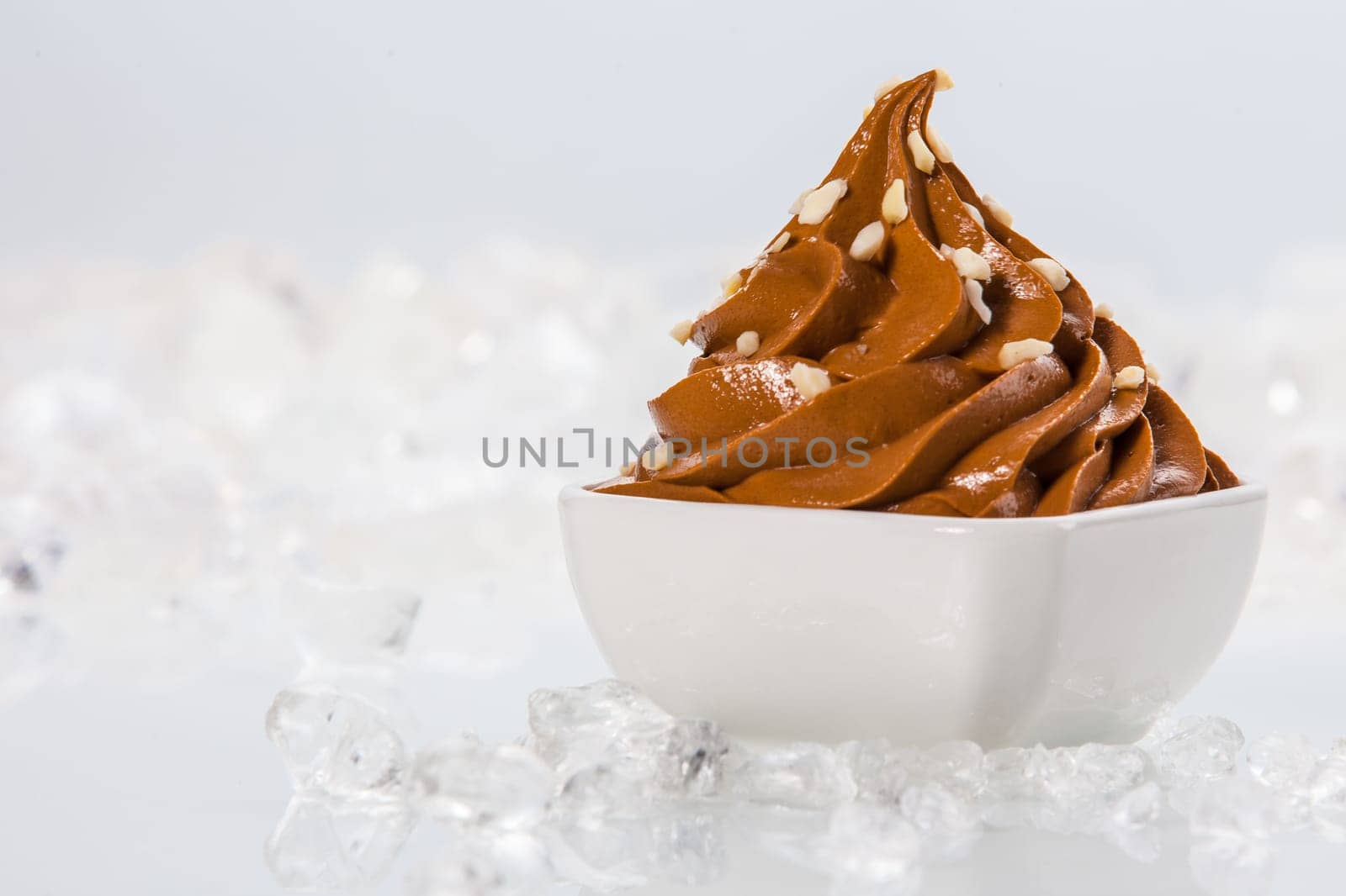 Tasty Brown Frozen Yogurt on White Bowl Surrounded by Ice on Table. Isolated on White Background.