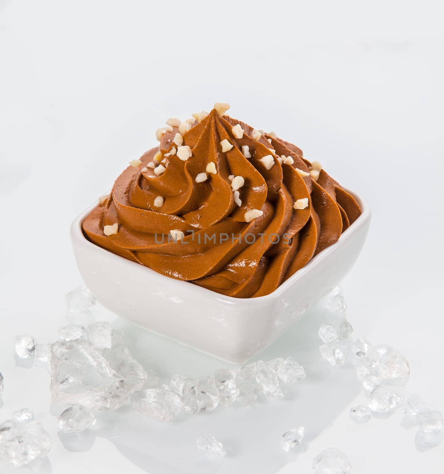 Close up Brown Frozen Yogurt on White Bowl with Little Toppings. Surrounded by Ice Pieces. Isolated on White Background.
