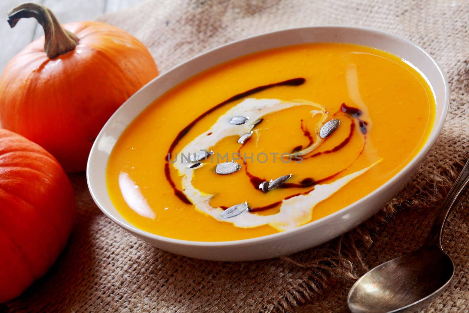 Creamy homemade bowl of pumpkin soup with fresh vegetable ingredients on hessian, closeup view