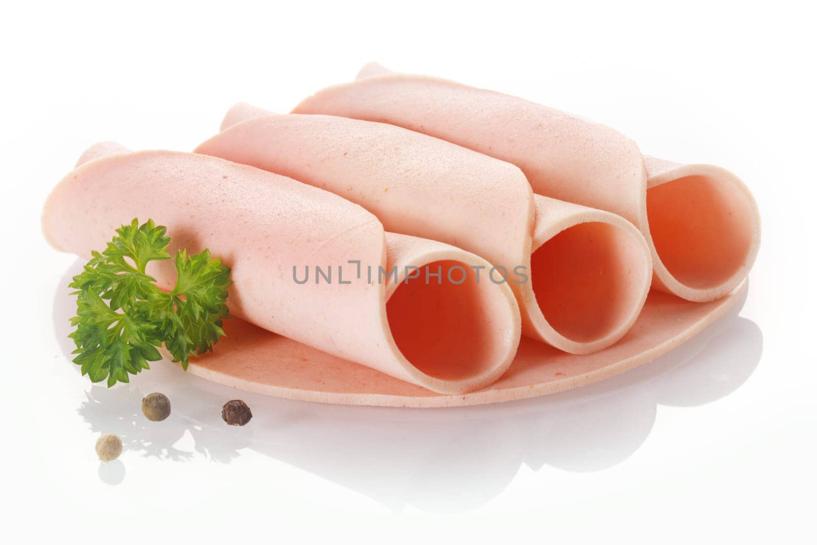 Three rolled slices of smoked processed ham or polony presented on a plate with fresh parsley and peppercorns over a white background