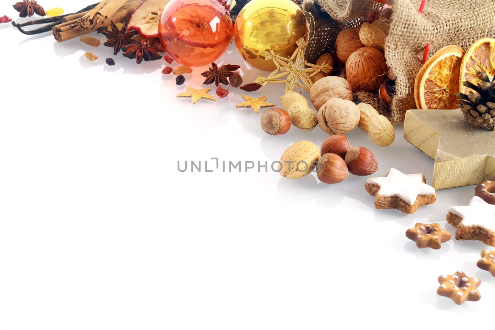 Christmas spices and nuts corner border with dried orange, vanilla pods, cinnamon, assorted nuts, star-shaped cookies and star anise over white with copyspace for your seasonal message