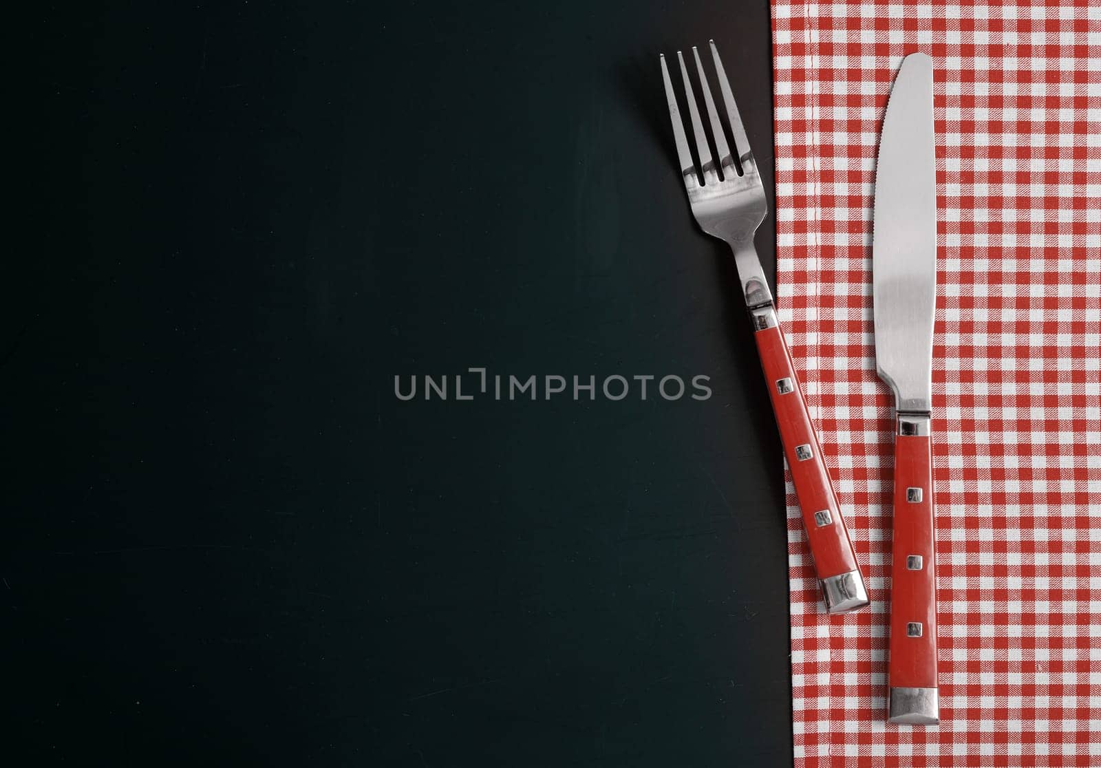Fork and Knife on Checked Table Cloth at Black Table.