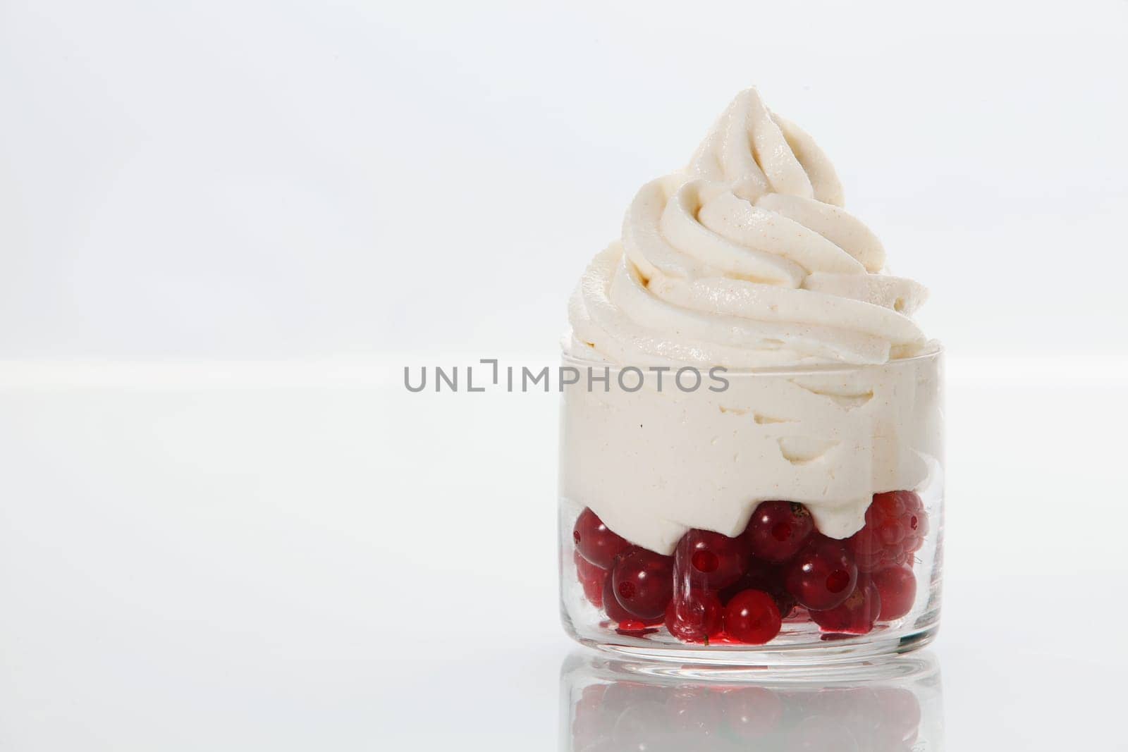 Ripe redcurrants topped with vanilla frozen yogurt served as a party dessert in a glass dish on a white table with copyspace