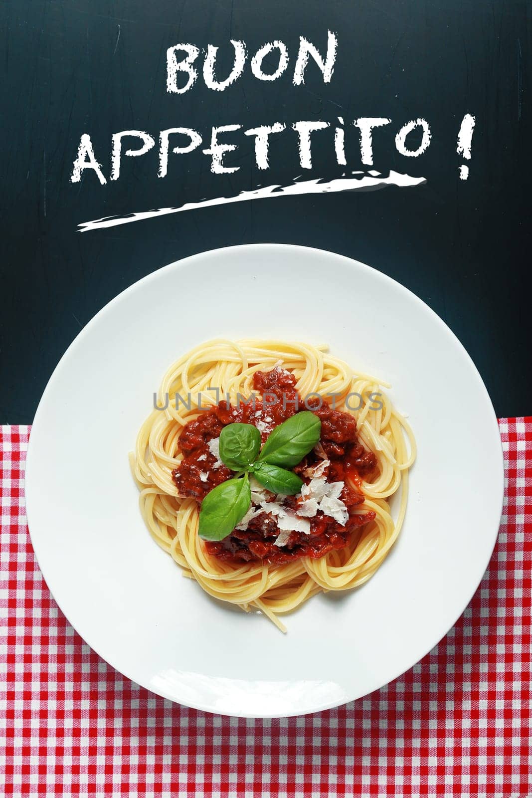 Overhead view of a plate of spaghetti Bolognaise or Bolognese under a Buon Appetito handwritten sign with a rich tomato and ground beef sauce garnished with basil and parmesan cheese
