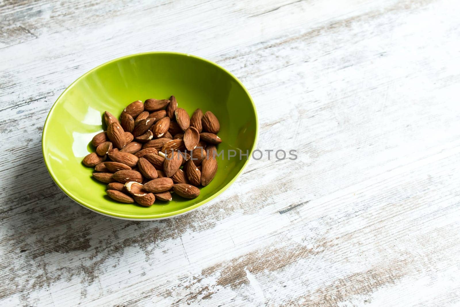 Almonds in a green bowl over a table.