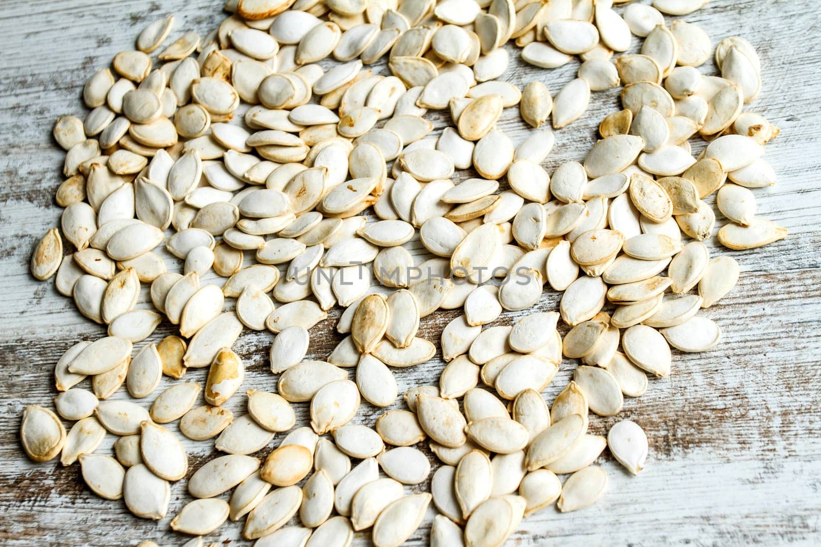 Many pumpkin seeds on a wooden table, background.