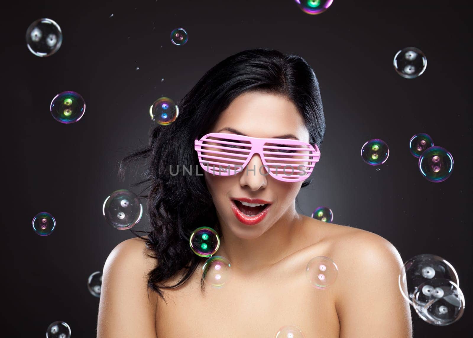 Young and happy woman wearing pink glasses surrounded by bubbles