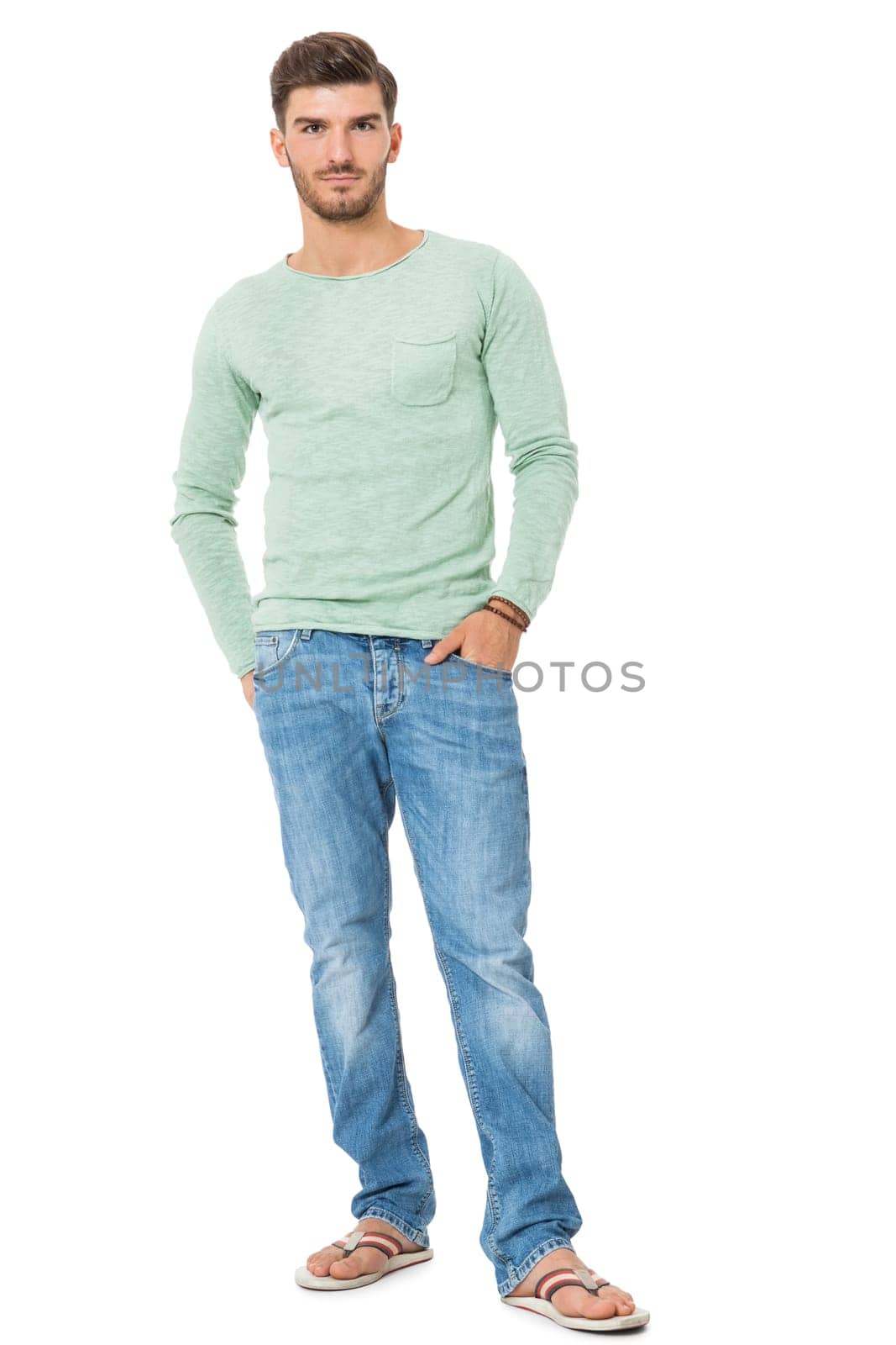 good-looking young man with beard posing with his hands in his pockets in jeans and sandals isolated on white background