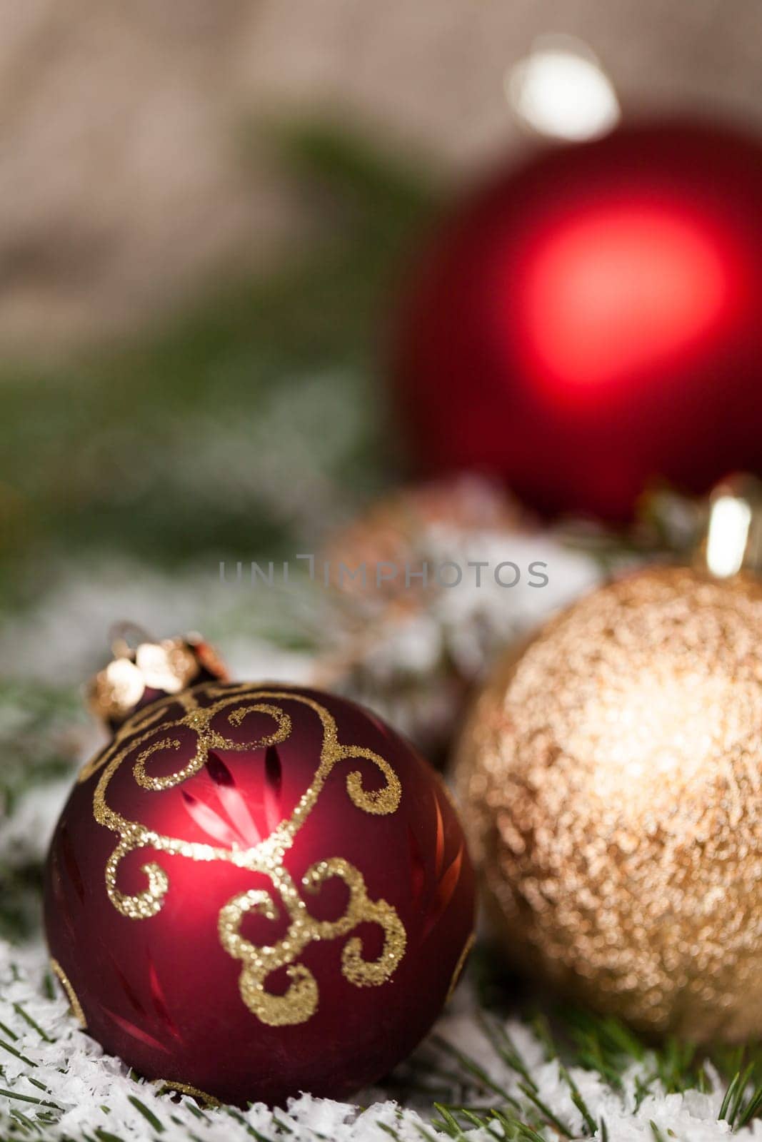 red Christmas baubles between cones and fir branches covered with snow as macro detail