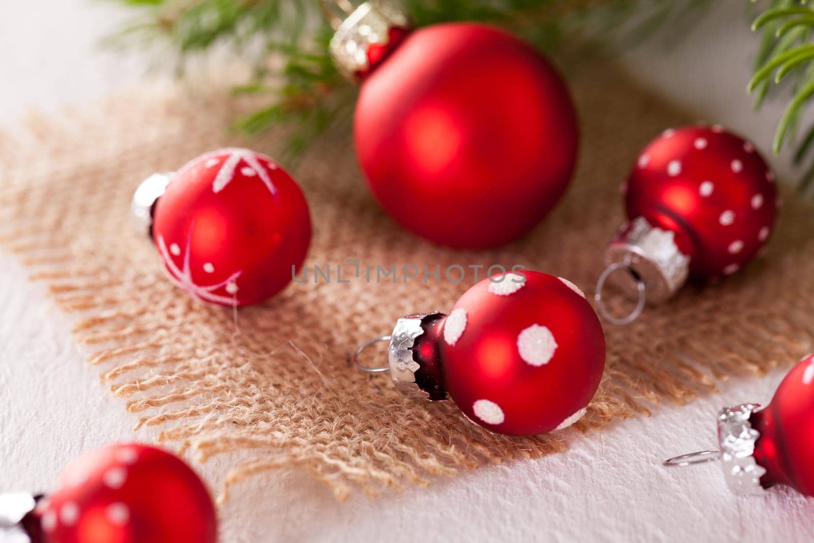 Beautiful red Christmas balls with small white dots with green fir branches on a jute sack