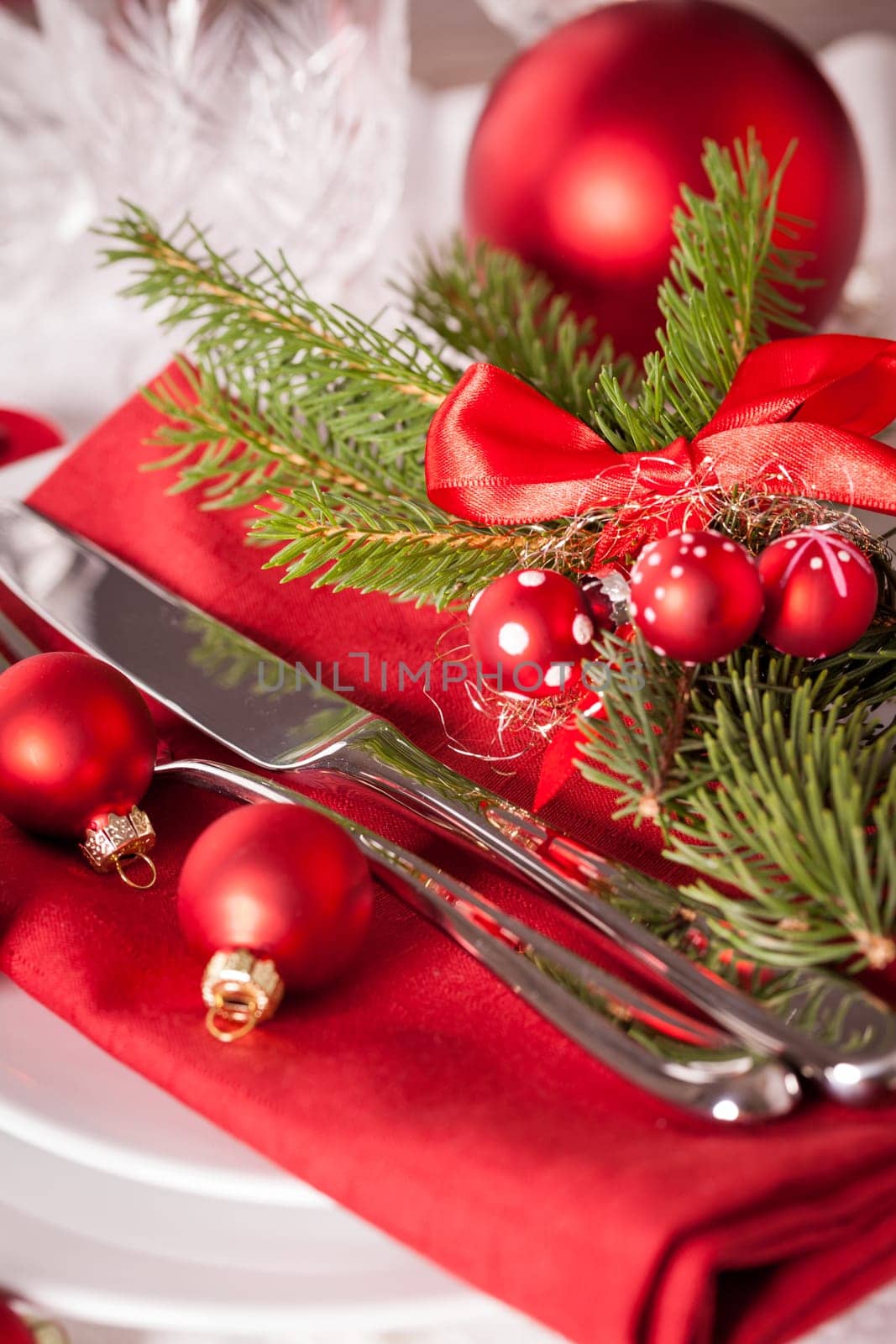 Red napkin with Christmas glass balls and cutlery with a green fir branch and red bow close-up