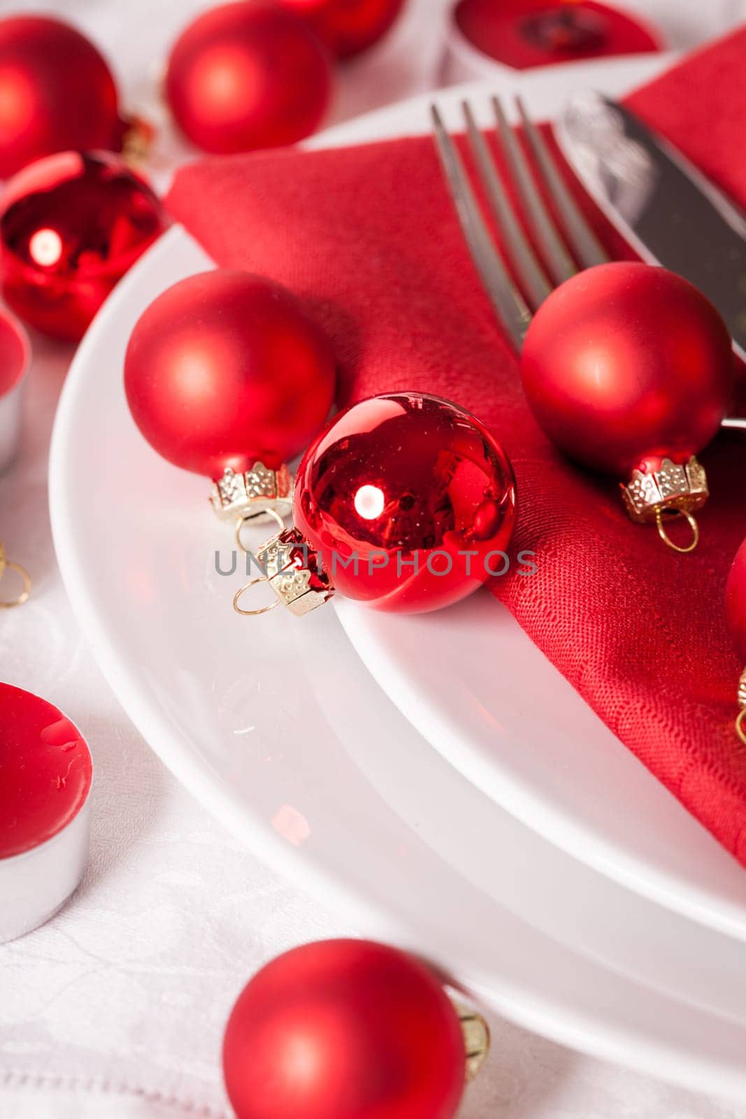 Red napkin with Christmas glass balls and cutlery with a green fir branch and red bow close-up