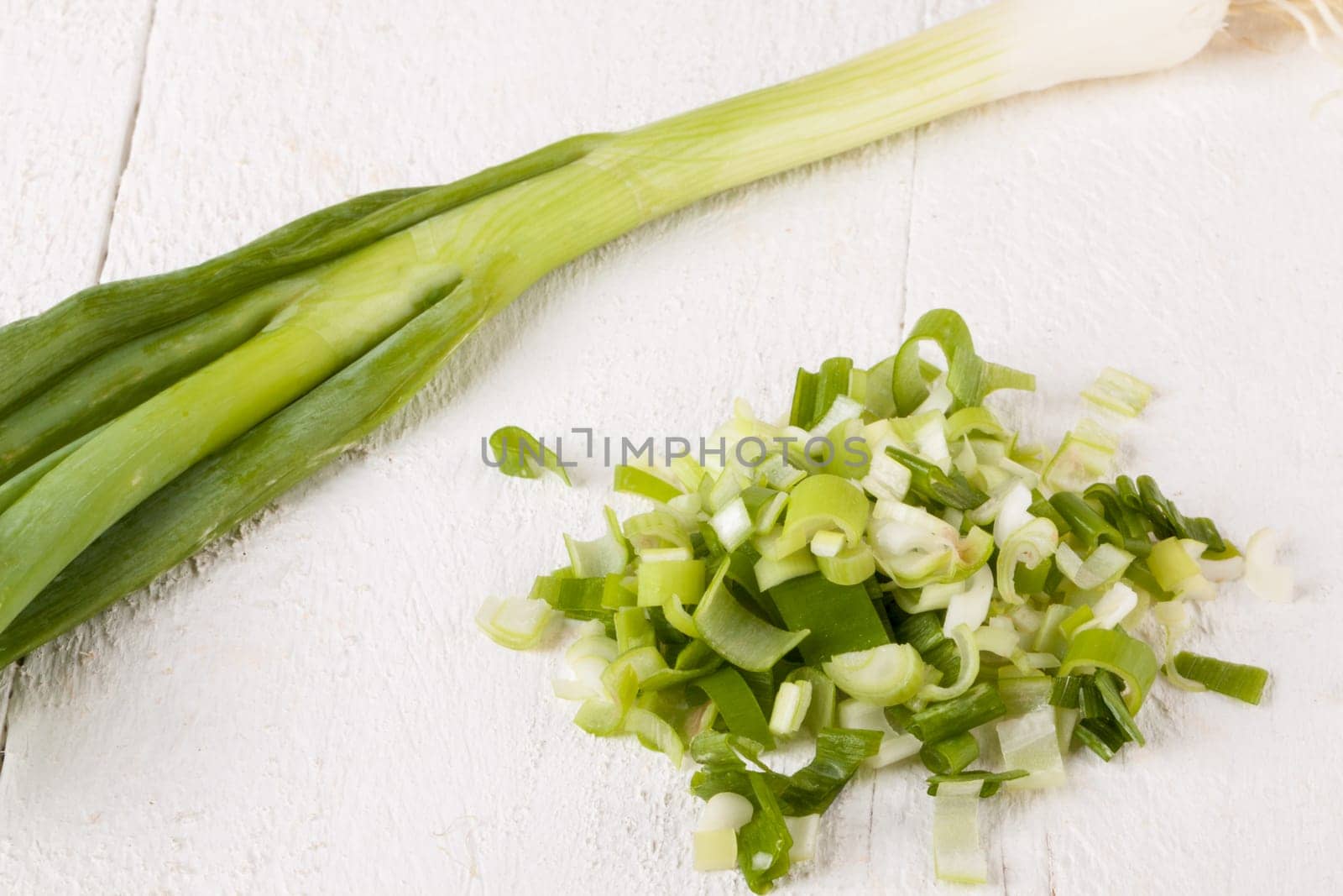 Leek spring onions with root as a whole and cut as a close-up on a white wooden board
