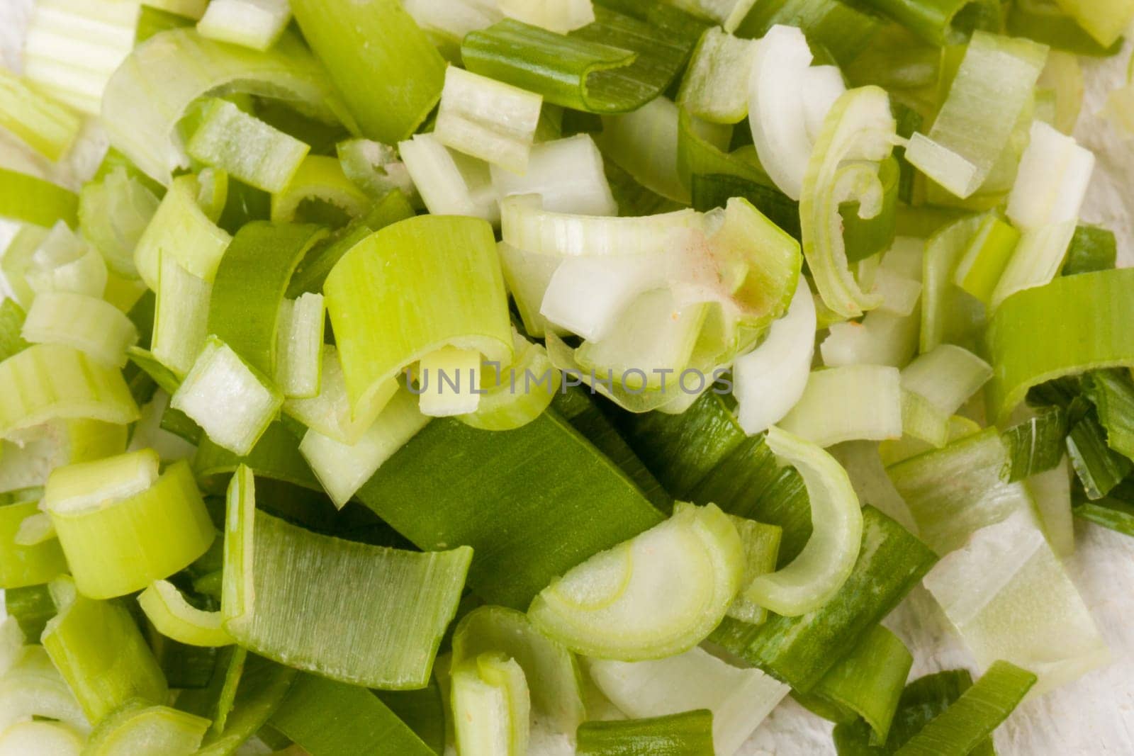 Leek spring onions with root as a whole and cut as a close-up on a white wooden board