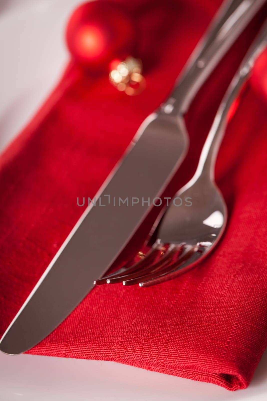Red napkin with Christmas glass balls and cutlery with a green fir branch and red bow close-up