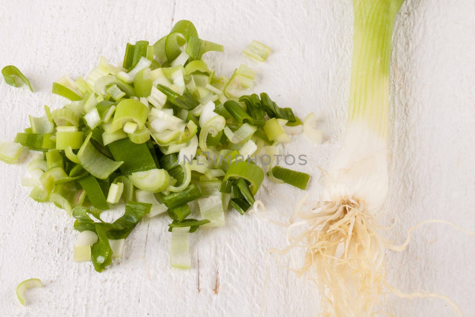 Leek spring onions with root as a whole and cut as a close-up on a white wooden board