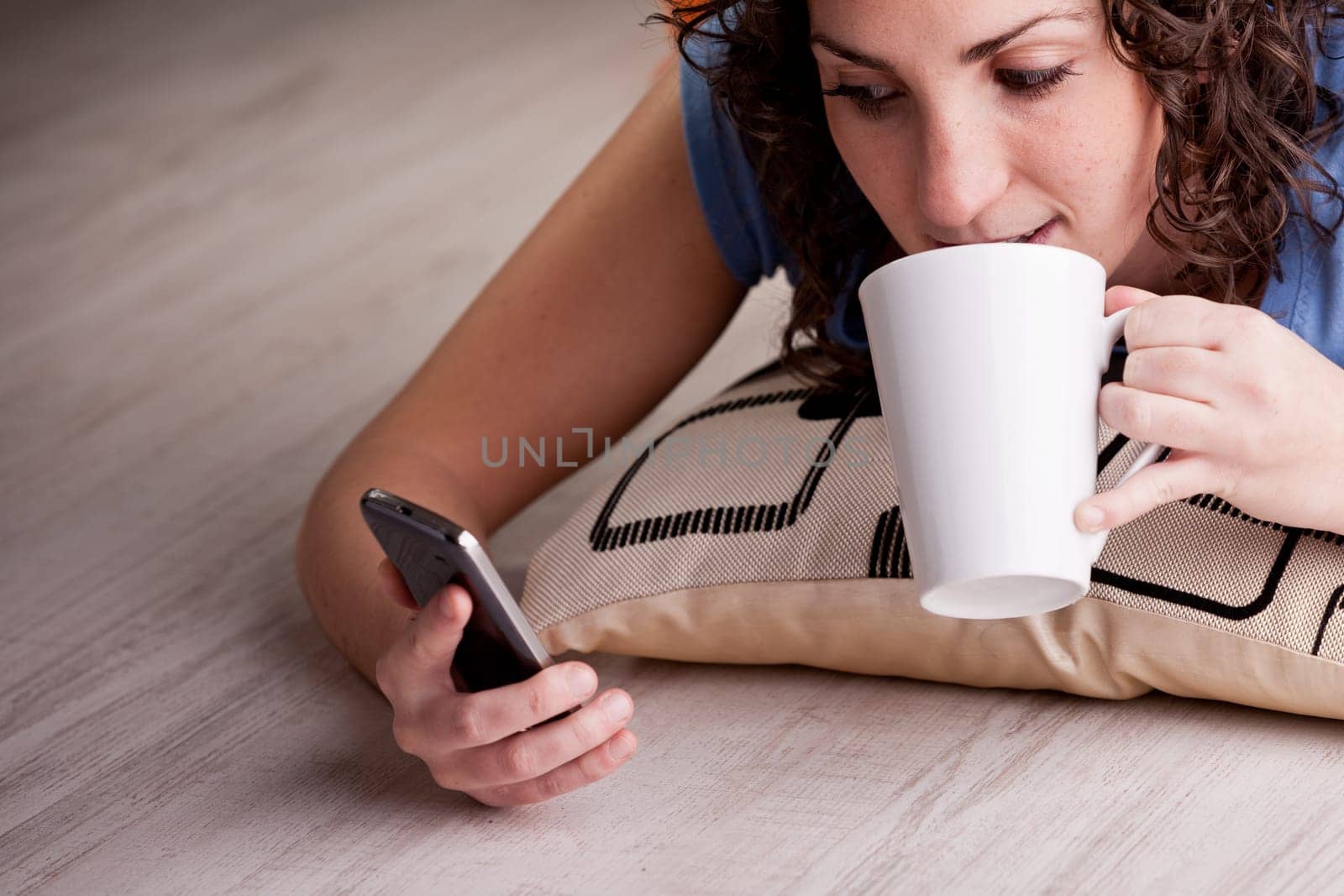 girl texting with her smartphone drinking a hot drink from her white mug