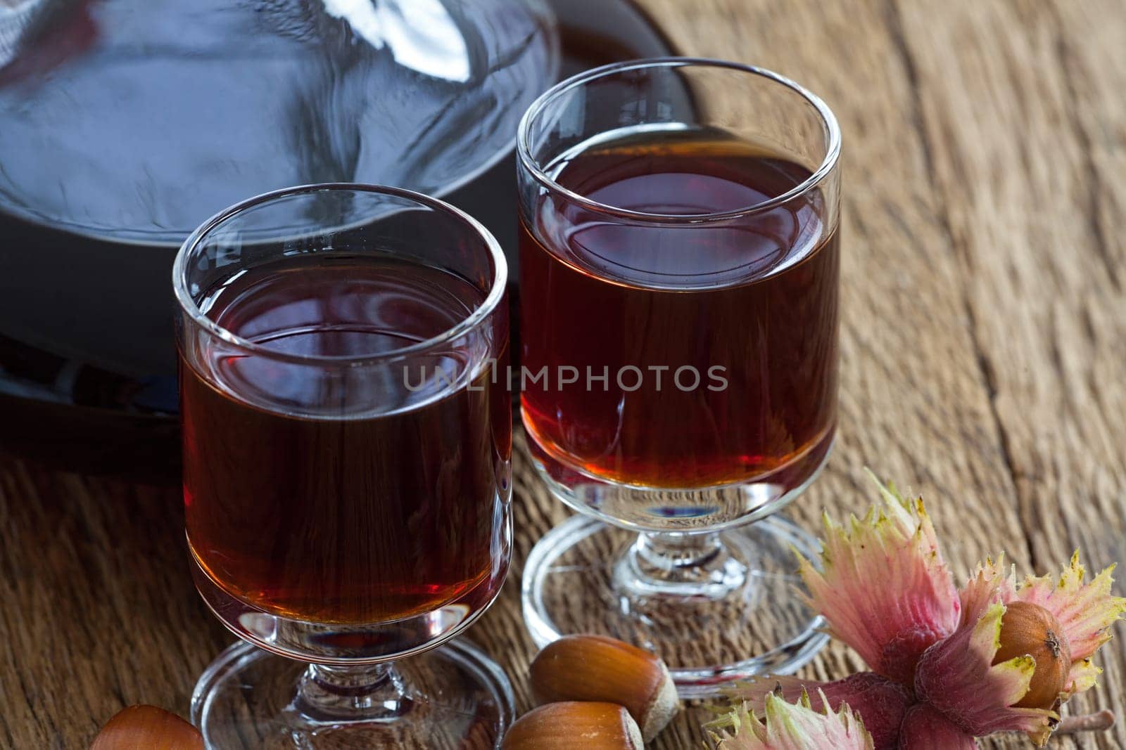 Close-up view of homemade hazelnut liqueur in a carafe and a glass with hazelnuts on wooden board