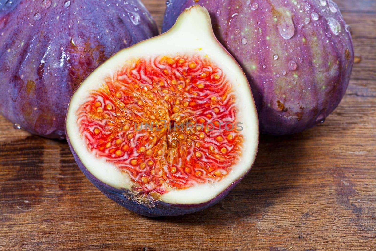 Two whole and one half fresh figs on old rustic wooden board