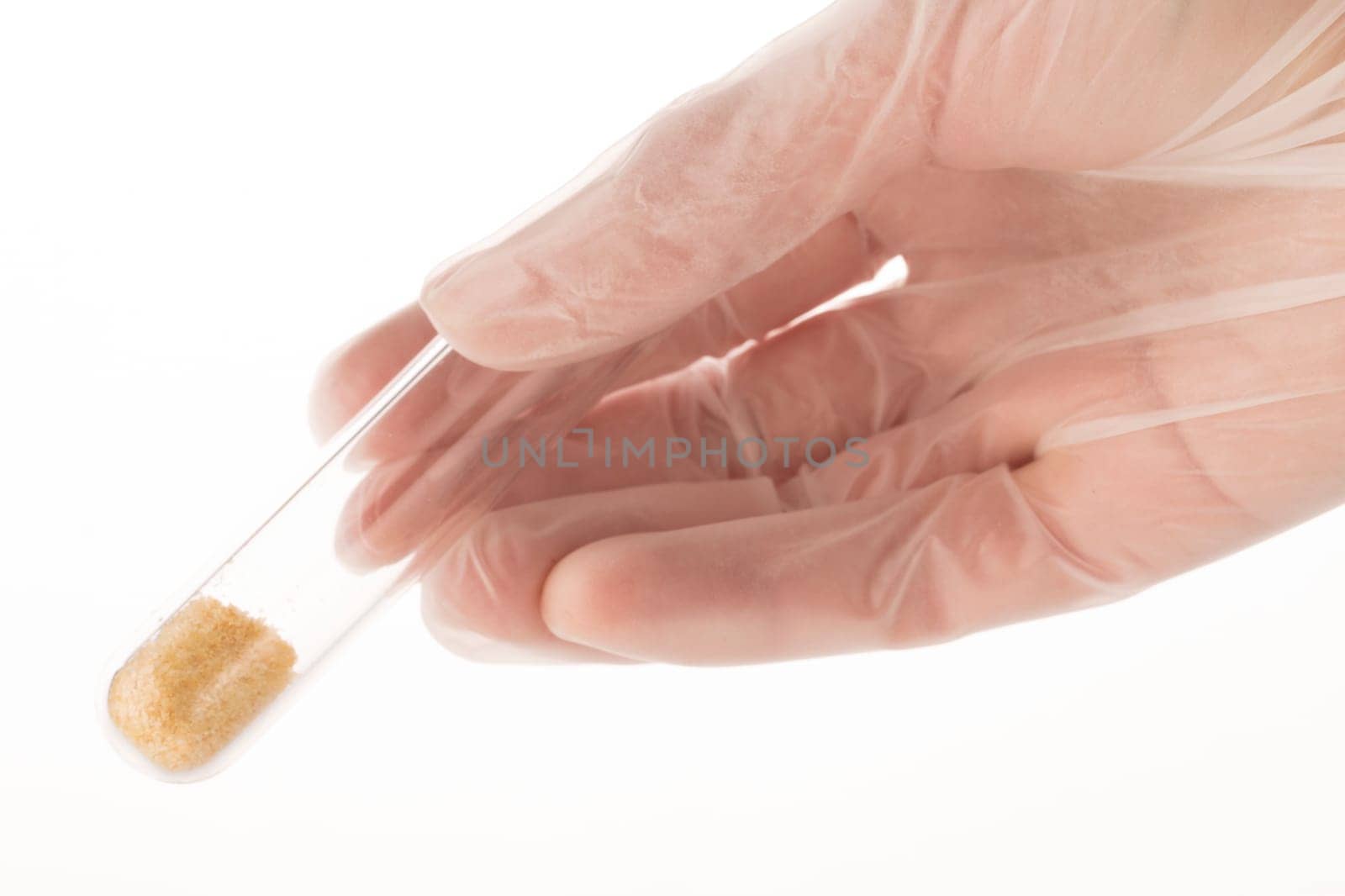 Gloved hand holding test tube with brown grains on white background.
