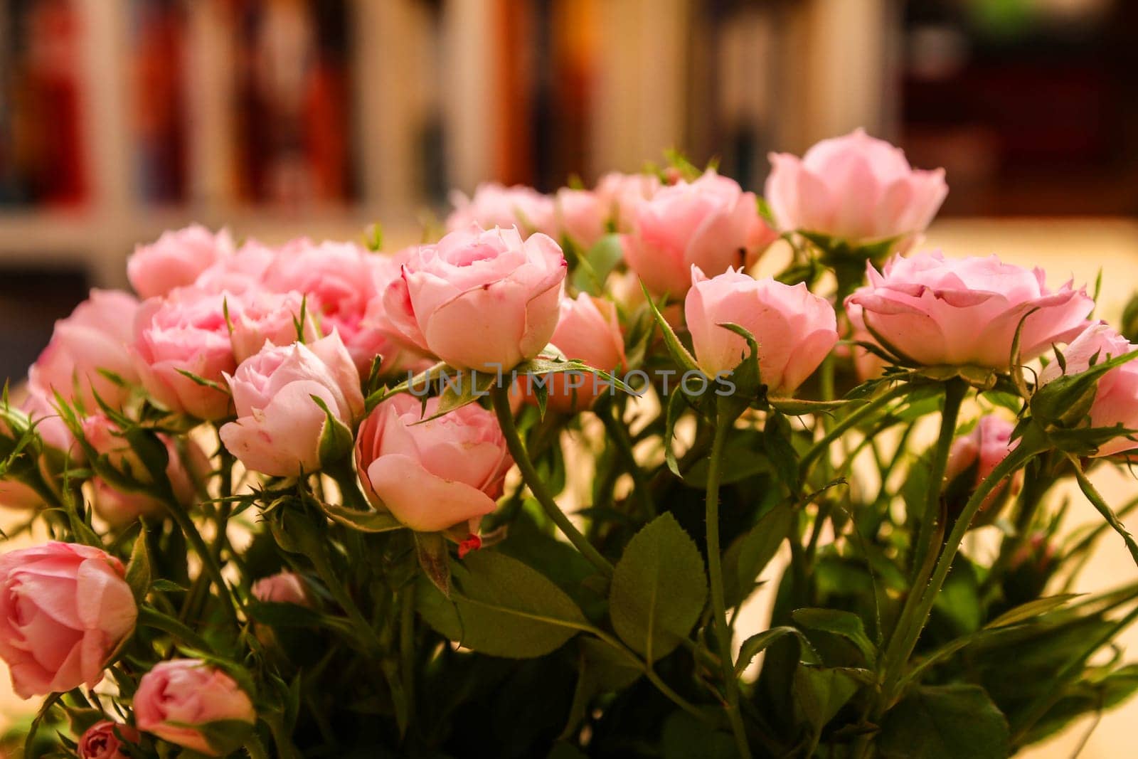 Bunch of small pink Roses in a glass vase over a wooden table..