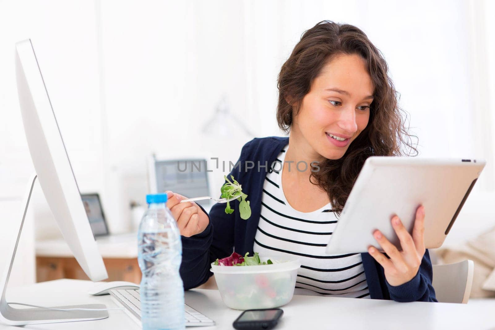 View of a Young attractive student eating salad while using tablet