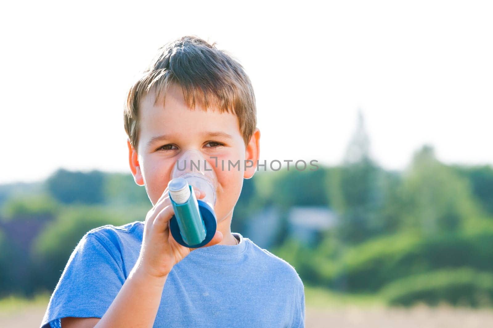Boy using inhaler for asthma in village with summer sunset