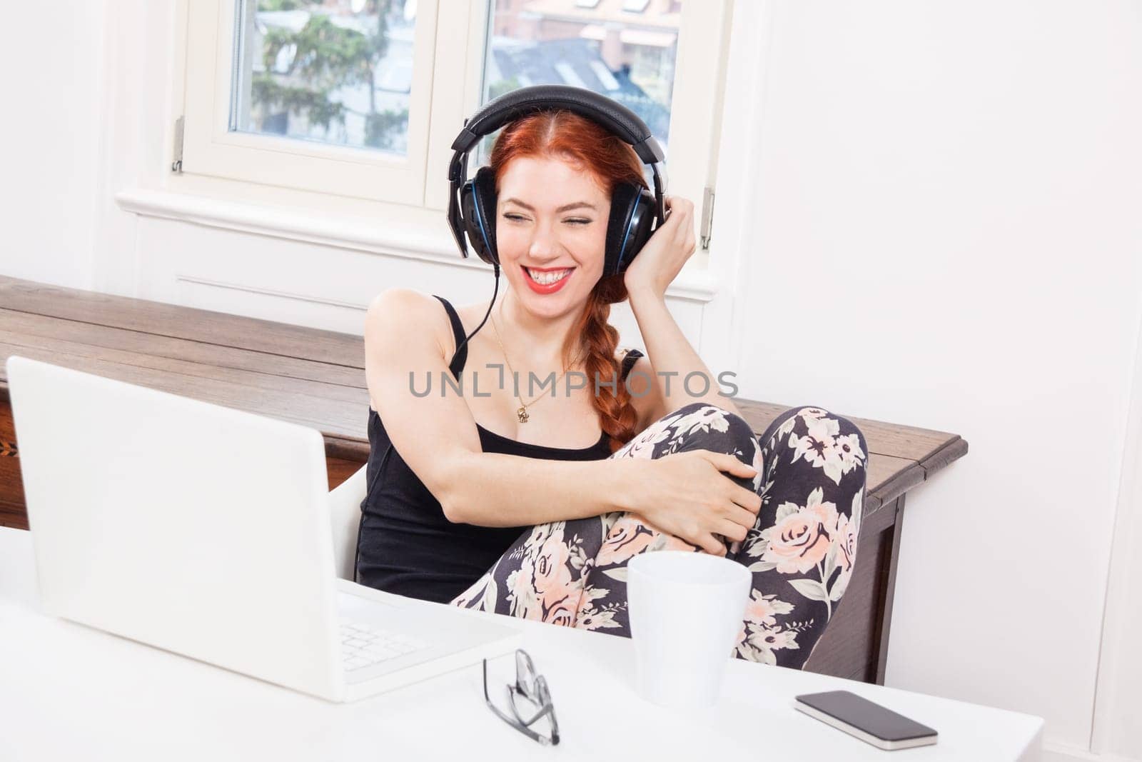 Young woman listens to music on computer with long red hair in living room