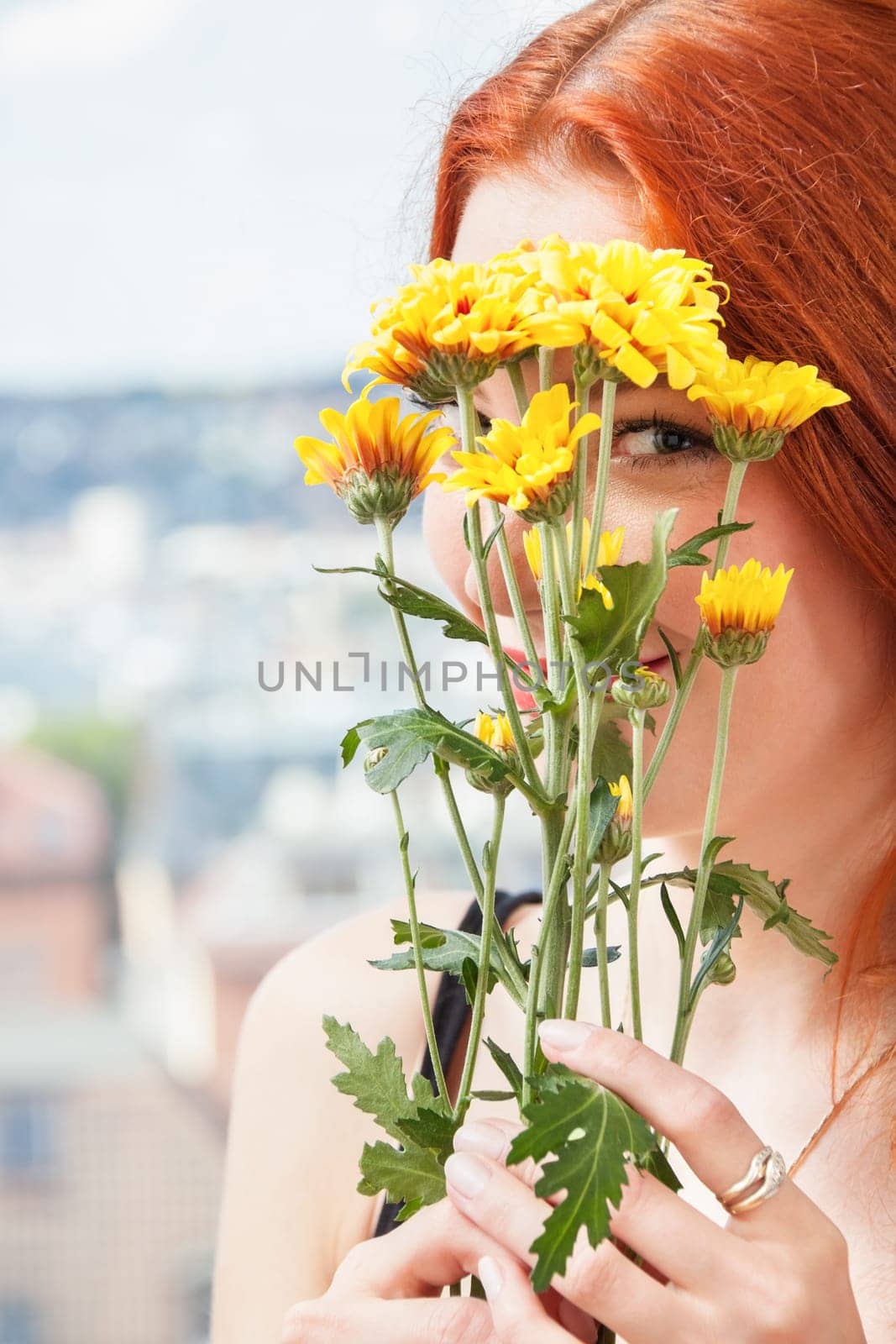 Thoughtful young woman looks out the window in summer with flowers in her hand