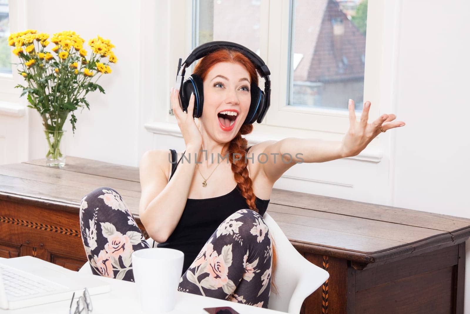 Young woman listens to music on computer with long red hair in living room