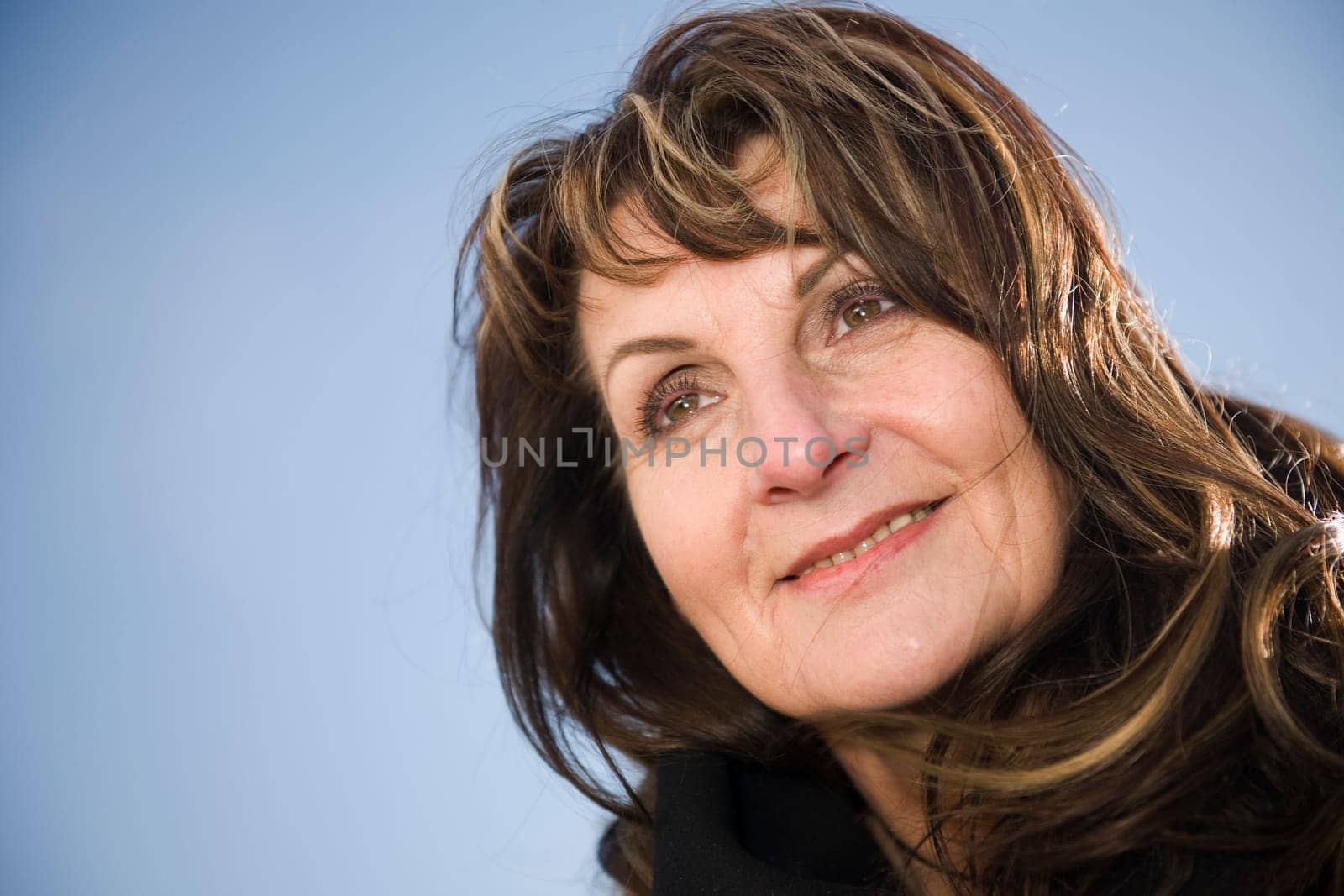 Head-port of a middle-aged woman looking happily to the side in front of blue sky