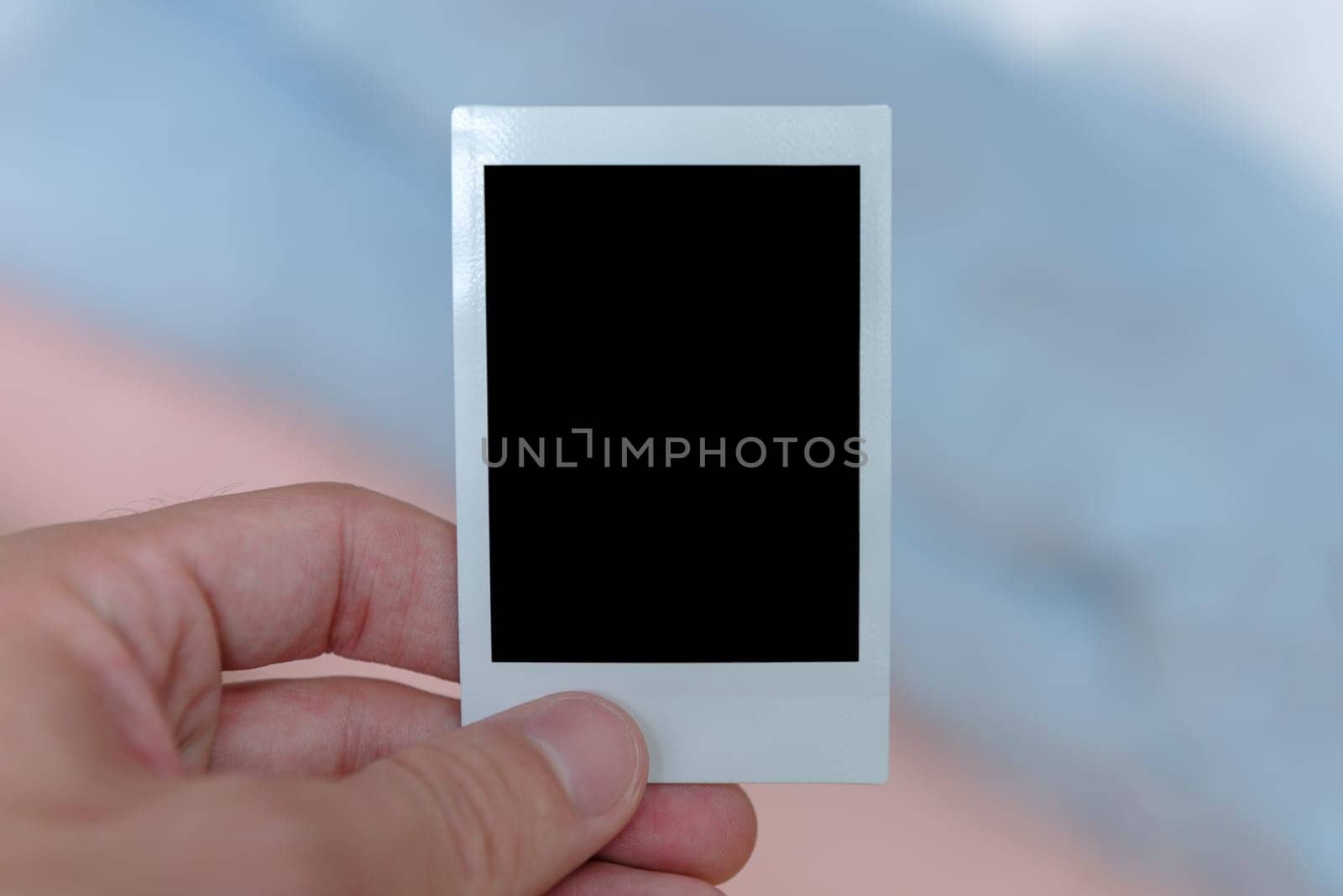 A man's hand holding an instant film print filled with a solid black space to customize with your own picture.