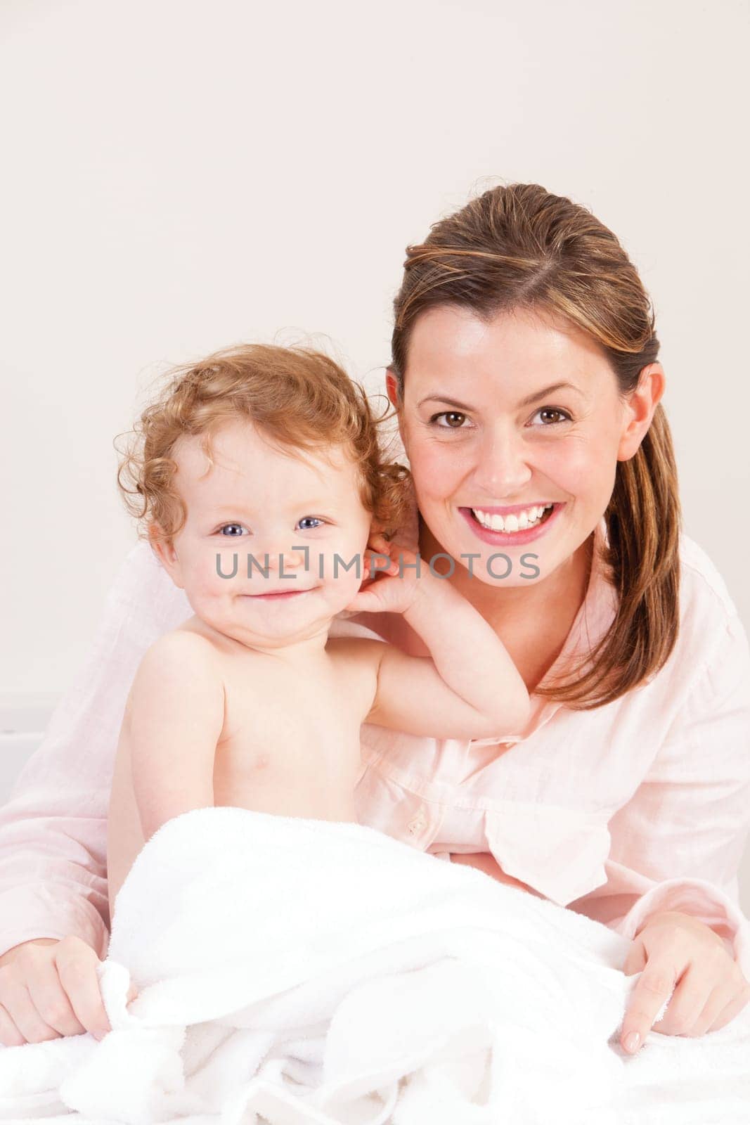 Little girl and her mother smiling at the camera whilst wrapped up in a towel