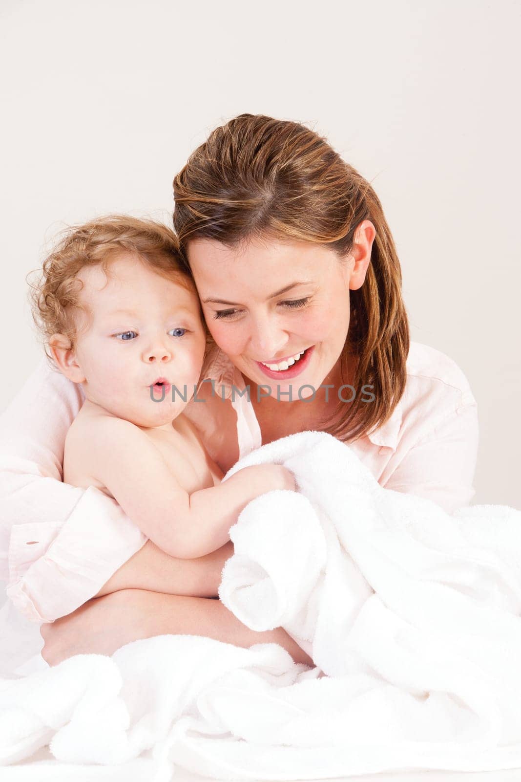 Mother playing with her baby daughter after a bath. There is a towel infront of them which the baby girl is holding.