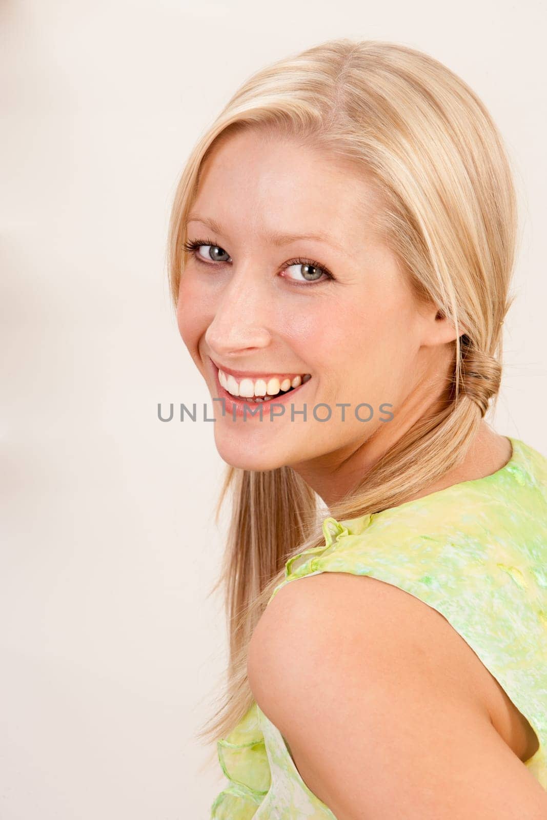 A beautiful young woman is looking over her shoulder and smiling for the camera. The background is plain.