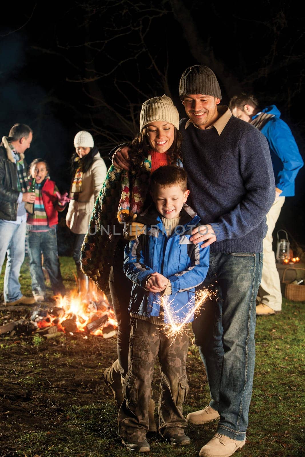 Little boy playing with a sparkler with his parents watching him