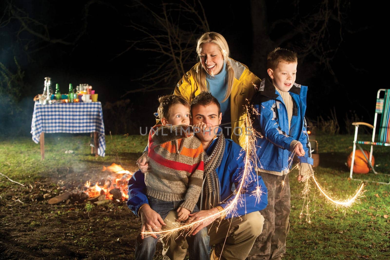 Brothers playing with sparklers in the garden with their mother and father