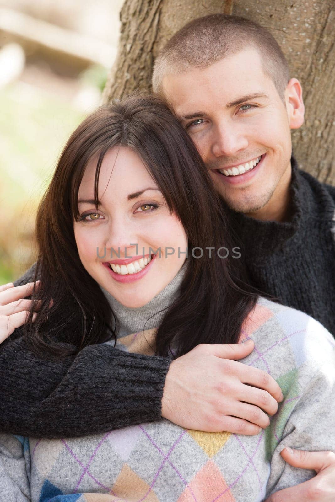 Attractive young couple cuddling out doors. They are both looking at the camera