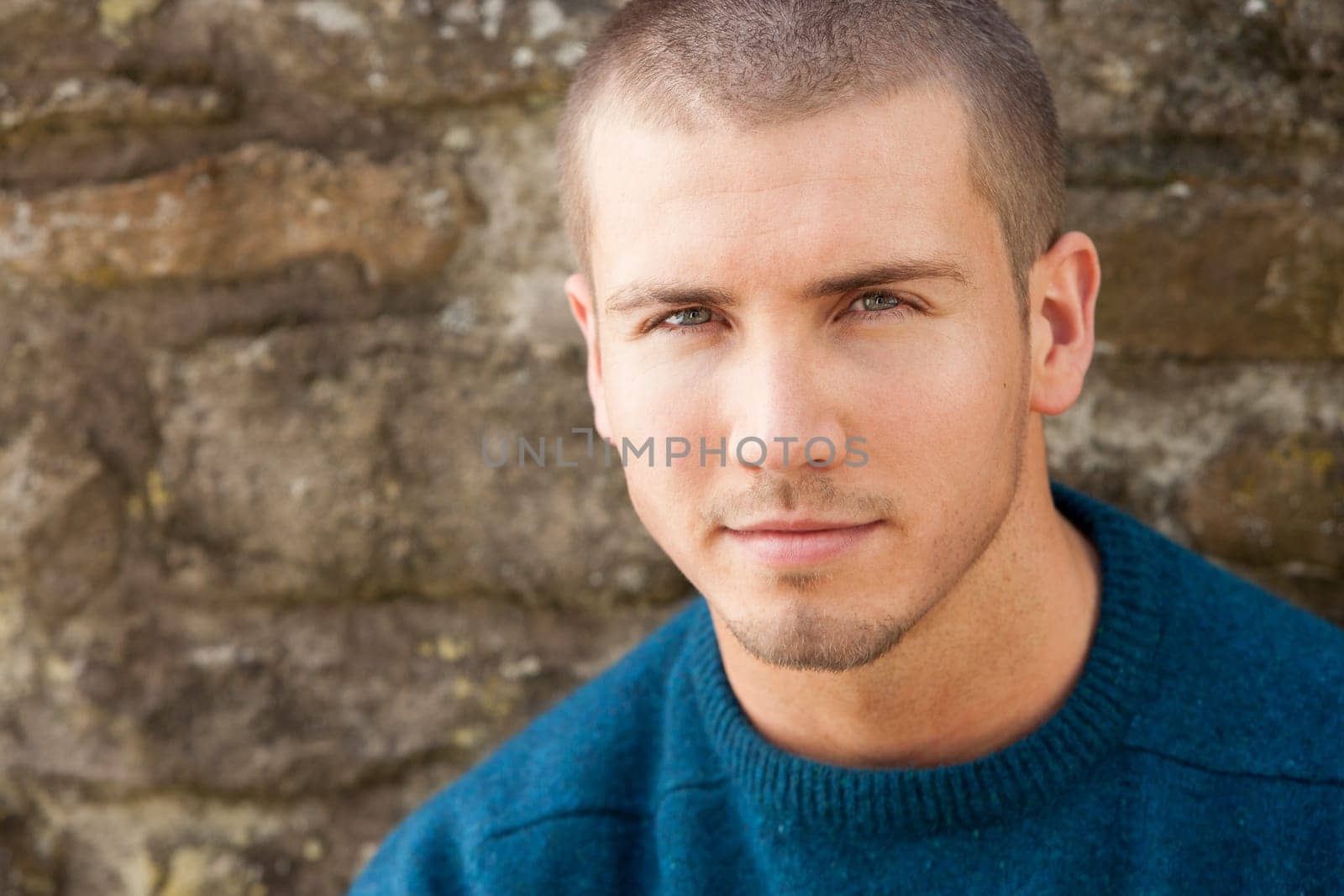 Attractive young man sitting outside. He is looking pensively at the camera.