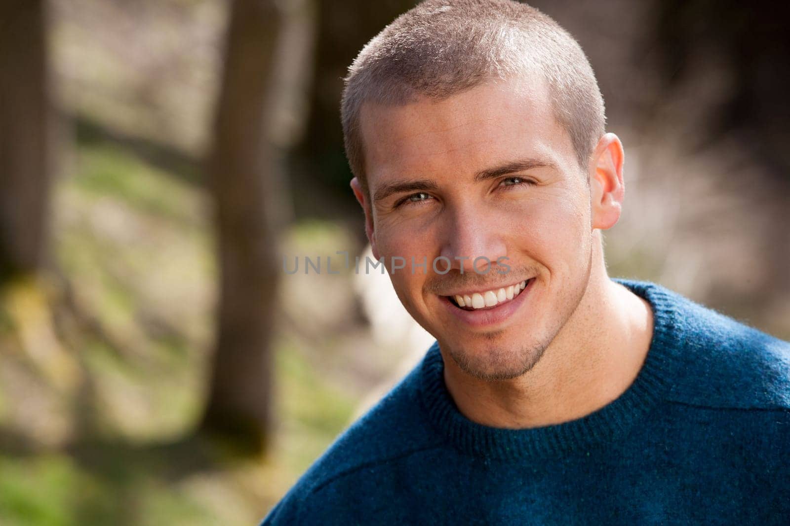 Attractive young man sitting outside. He is smiling at the camera.