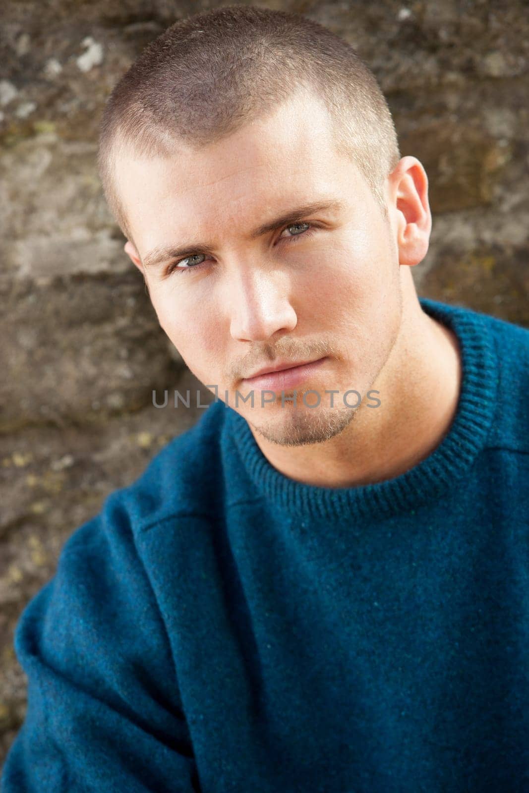 Attractive young man sitting outside. He is looking pensively at the camera.