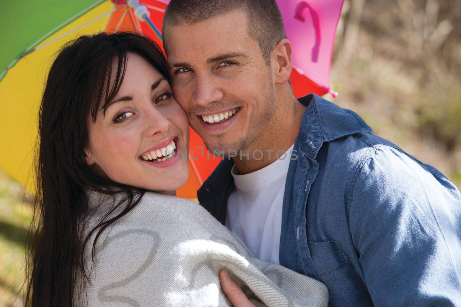 Attractive young couple cuddling out doors. They are both looking at the camera