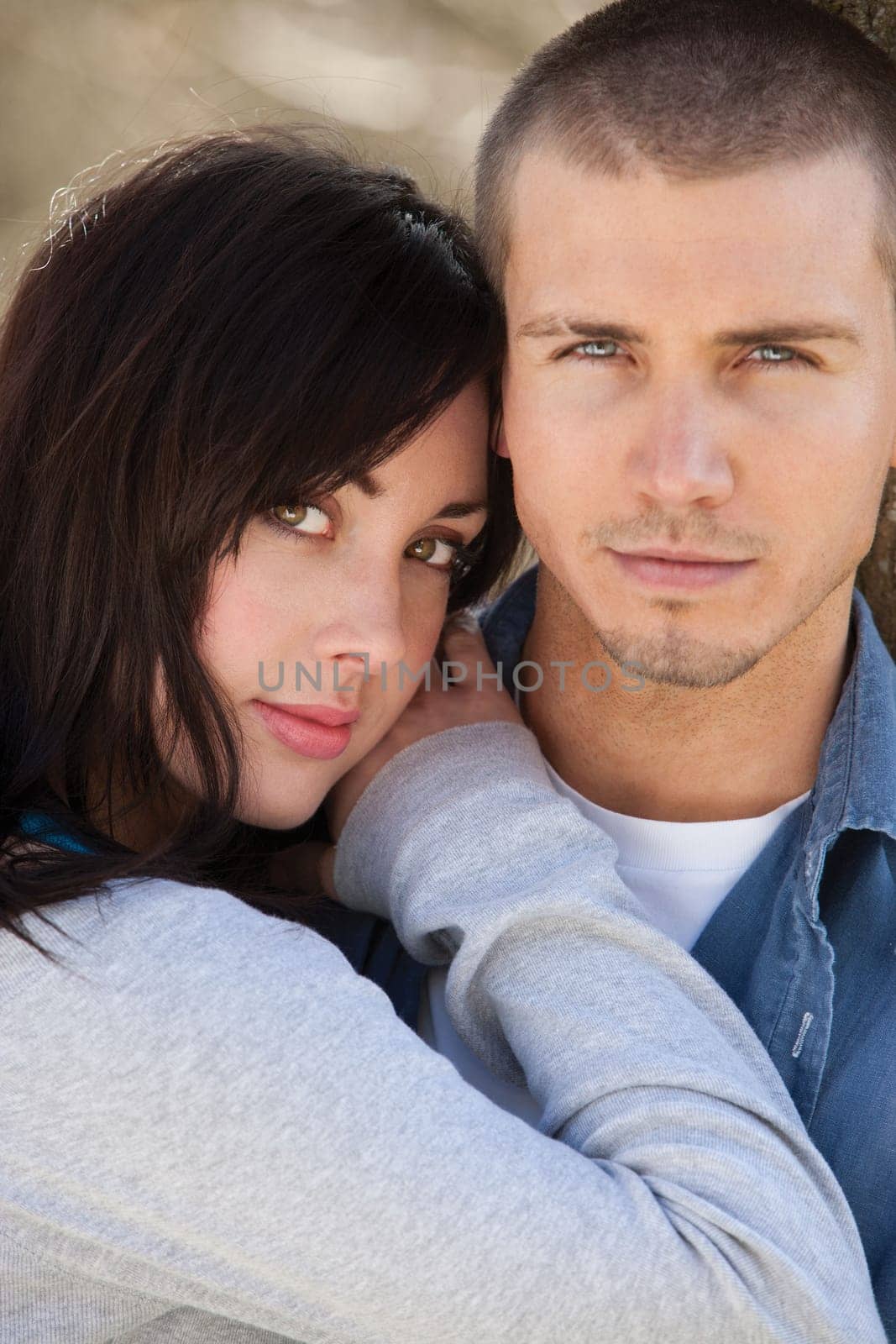 Attractive young couple cuddling outdoors. They are both looking at the camera