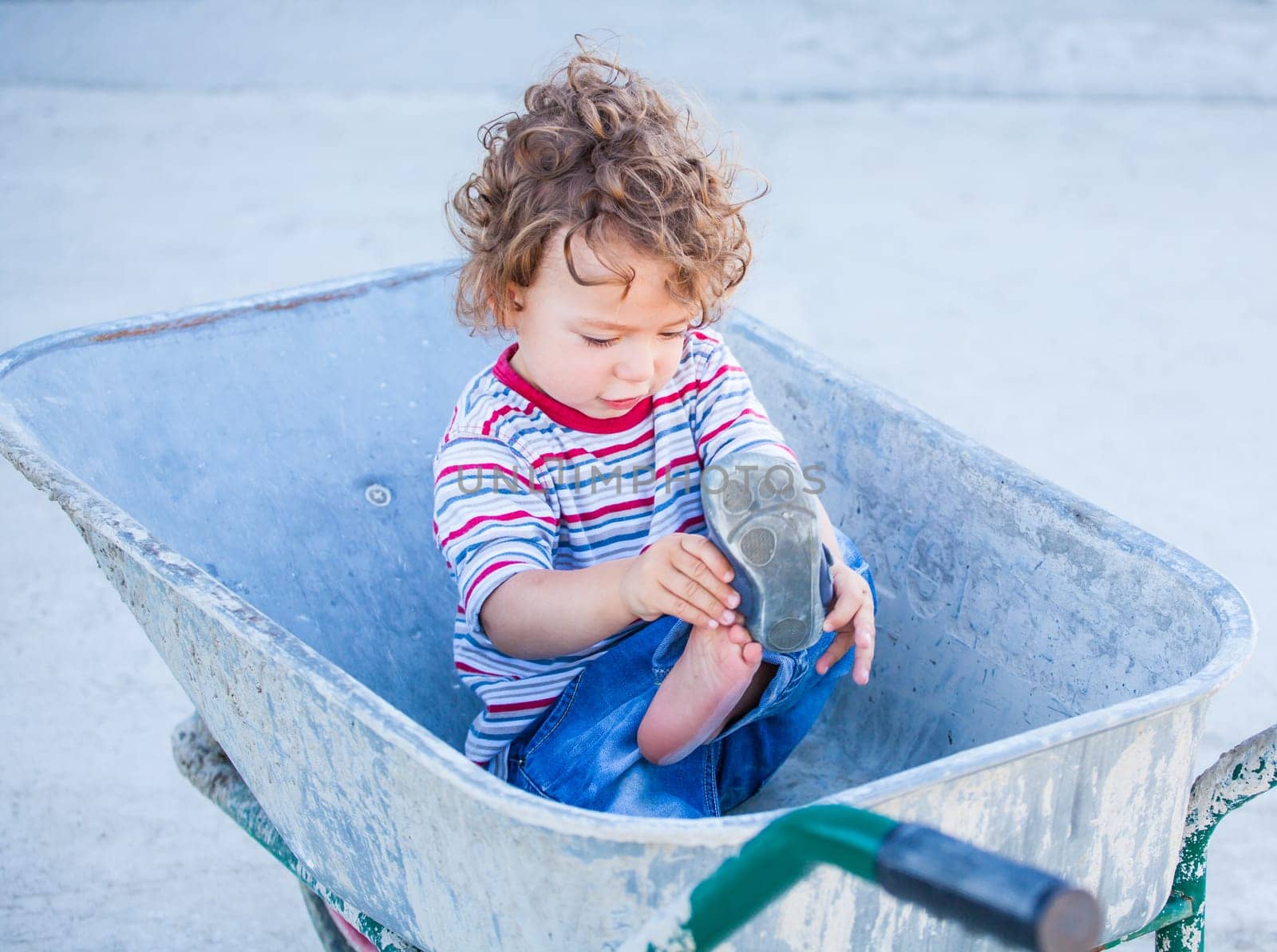 Portrait of 1 year old baby boy playing in a wheel barrow.