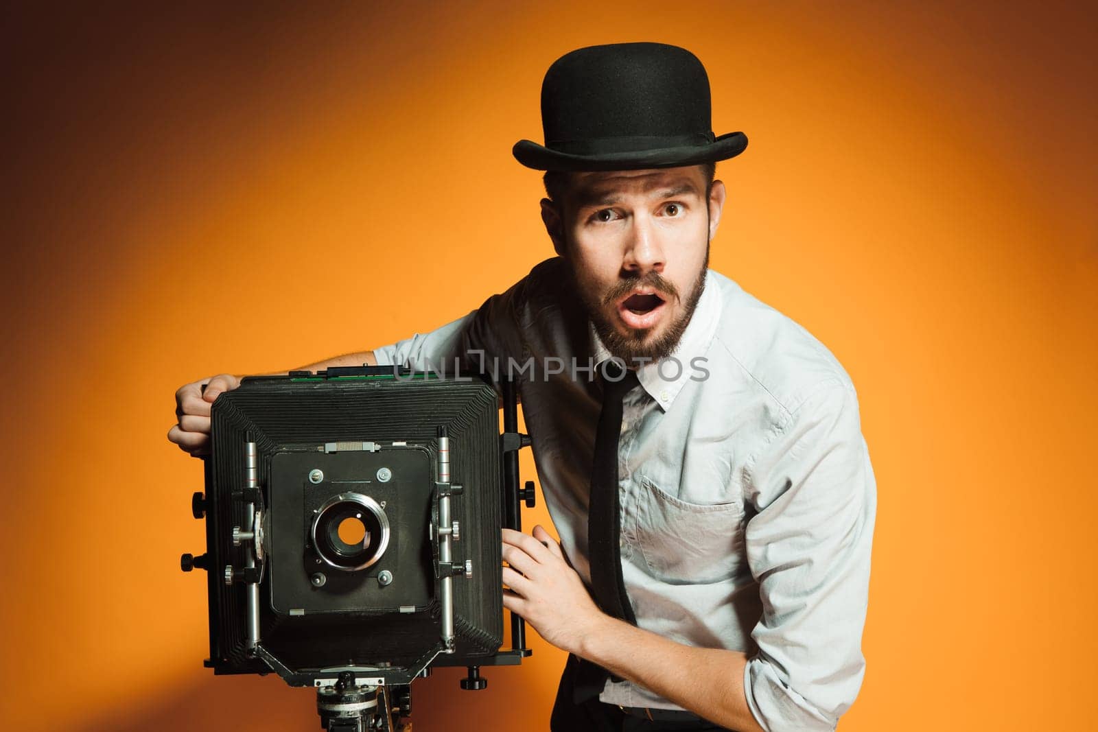 Young  afraid man in hat as photographer with retro camera on an orange background