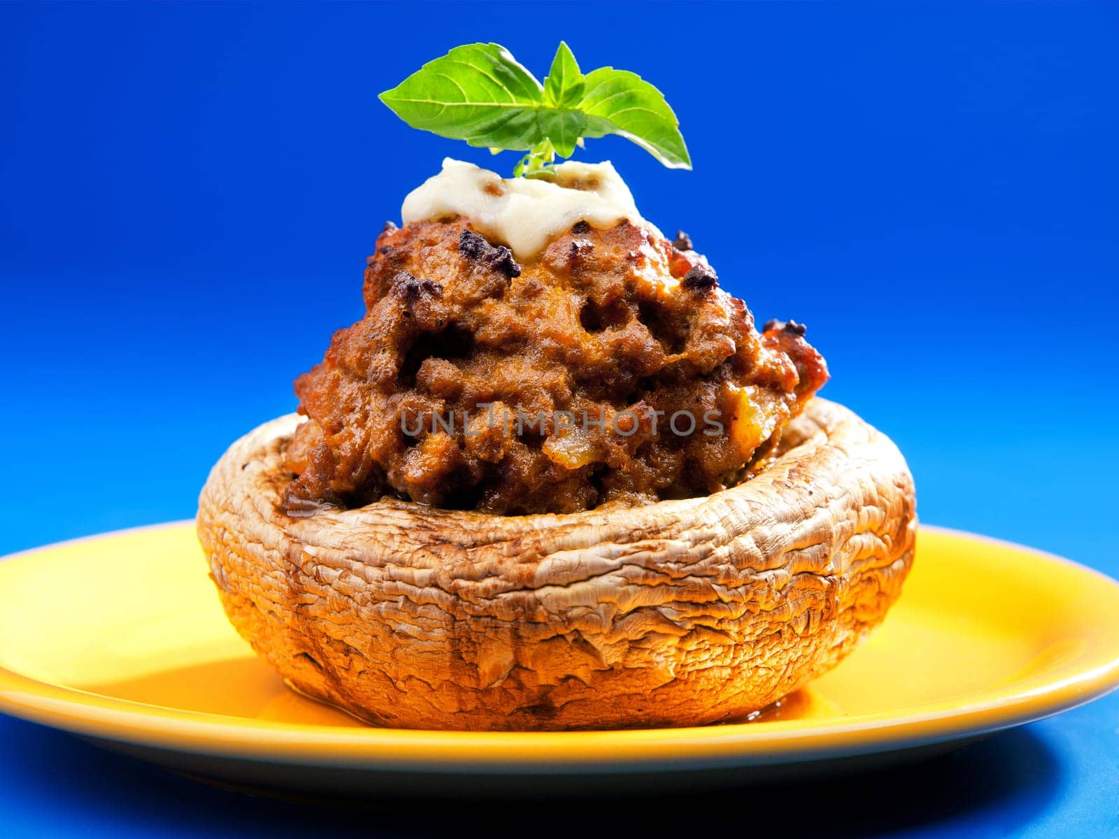 Stuffed mushrooms with meat and mozzarella decorated with fresh basil, izolated on green background