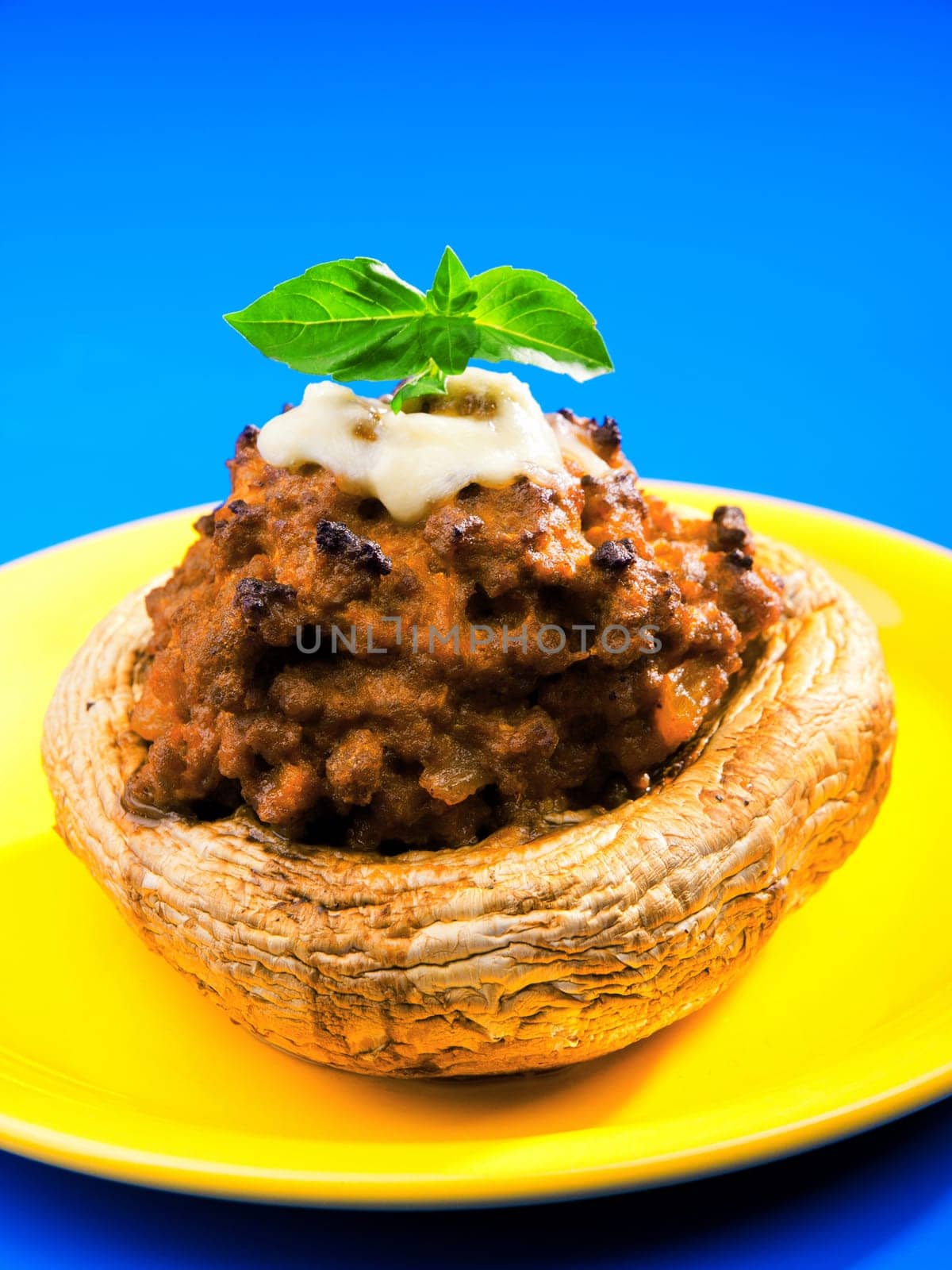 Stuffed mushrooms with meat and mozzarella decorated with fresh basil, isolated on green background